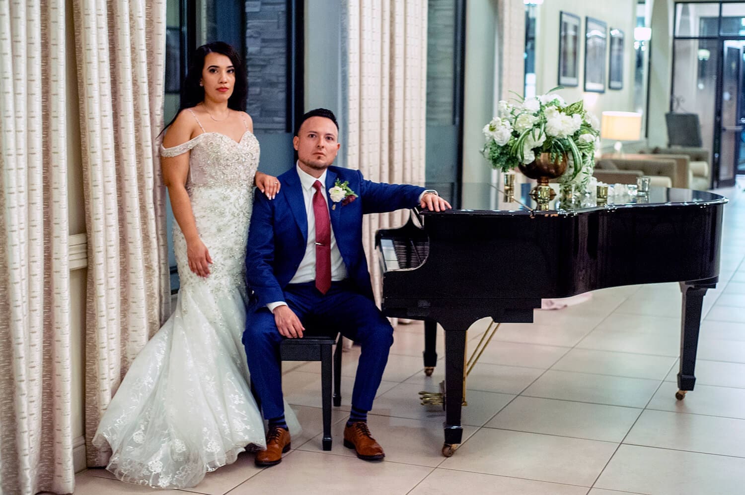 Bride and groom pose near a piano at their wedding reception venue