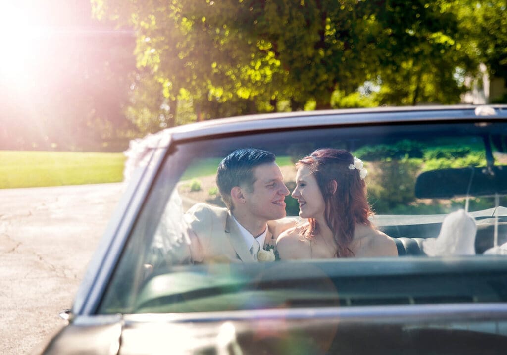 groom and bride take a photo in a vintage convertible during their wedding in Rockford, IL