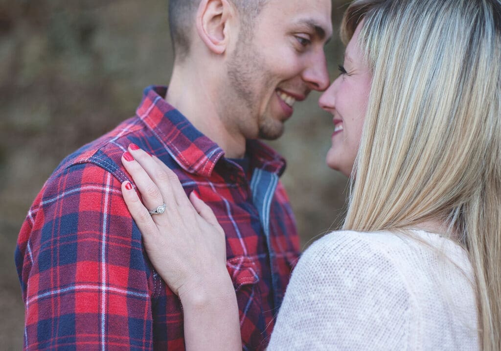 engaged couple pose with engagement ring in focus