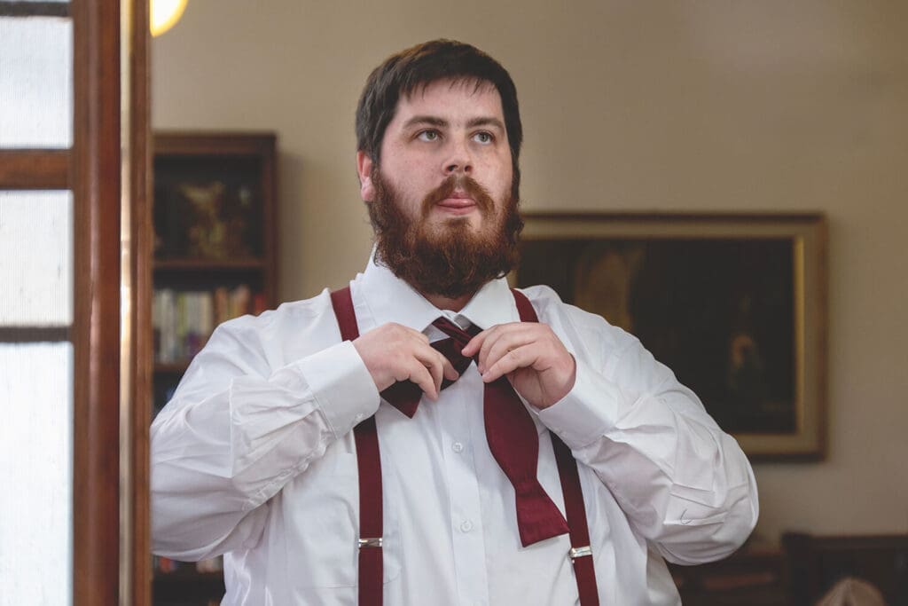 groom sticking tongue out while tying tie