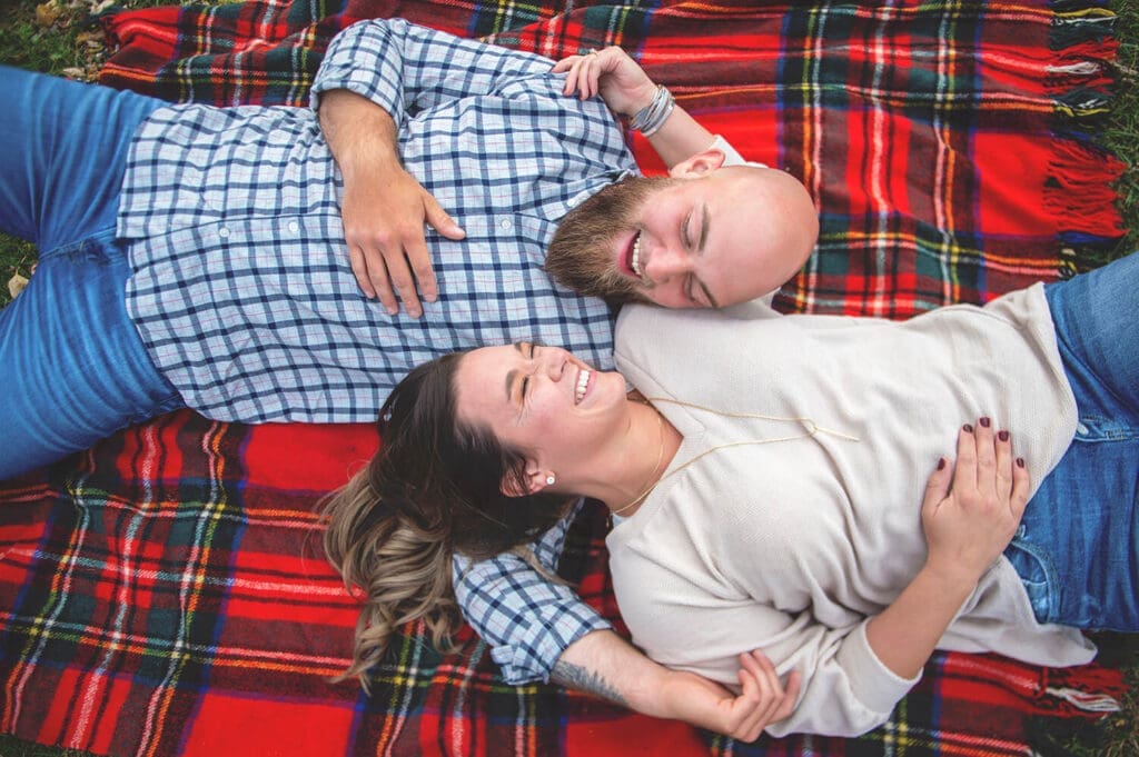 Engaged couple lay on plaid blanket at Beckman Mill in Beloit, WI