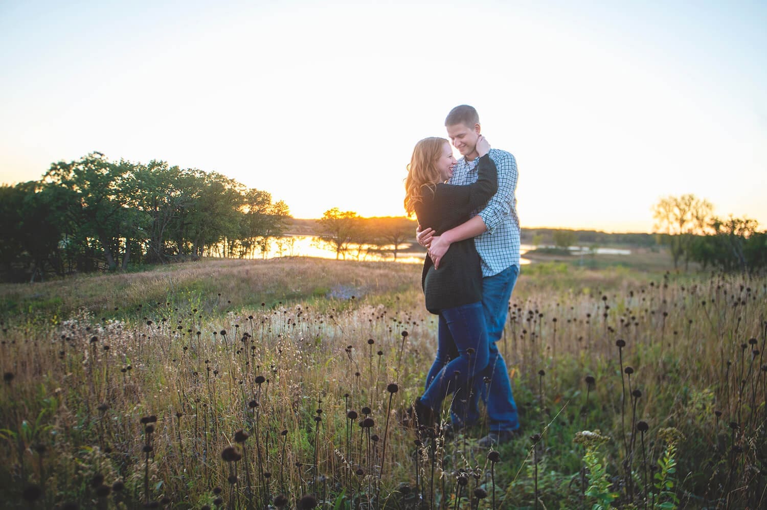 Engaged couple embrace during golden hour in open field