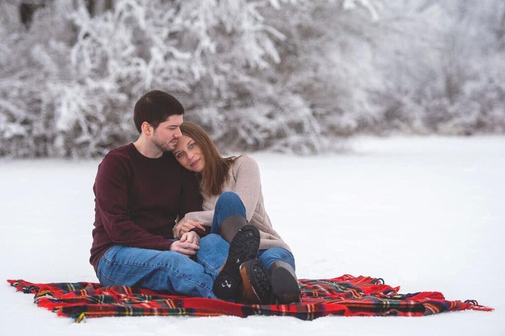 Engaged couple embrace on blanket in snow during engagement session in Northern Illinois