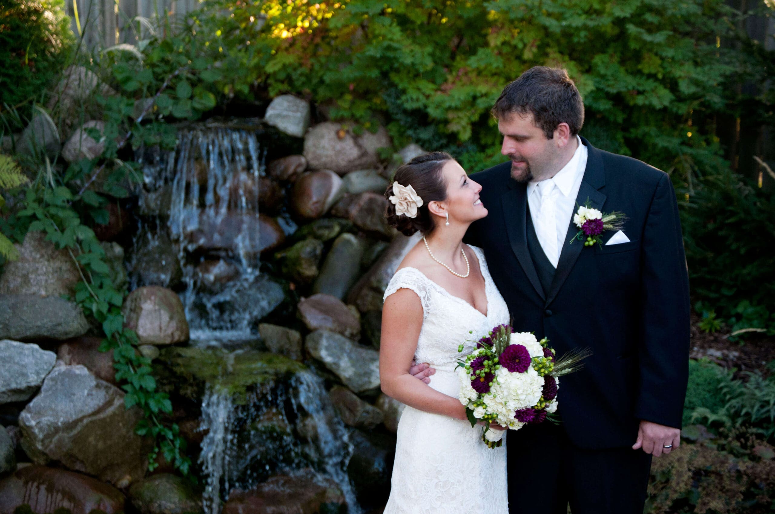 Wedding couple stand in front of the waterfall at Williams Tree Farm in Rockton, IL